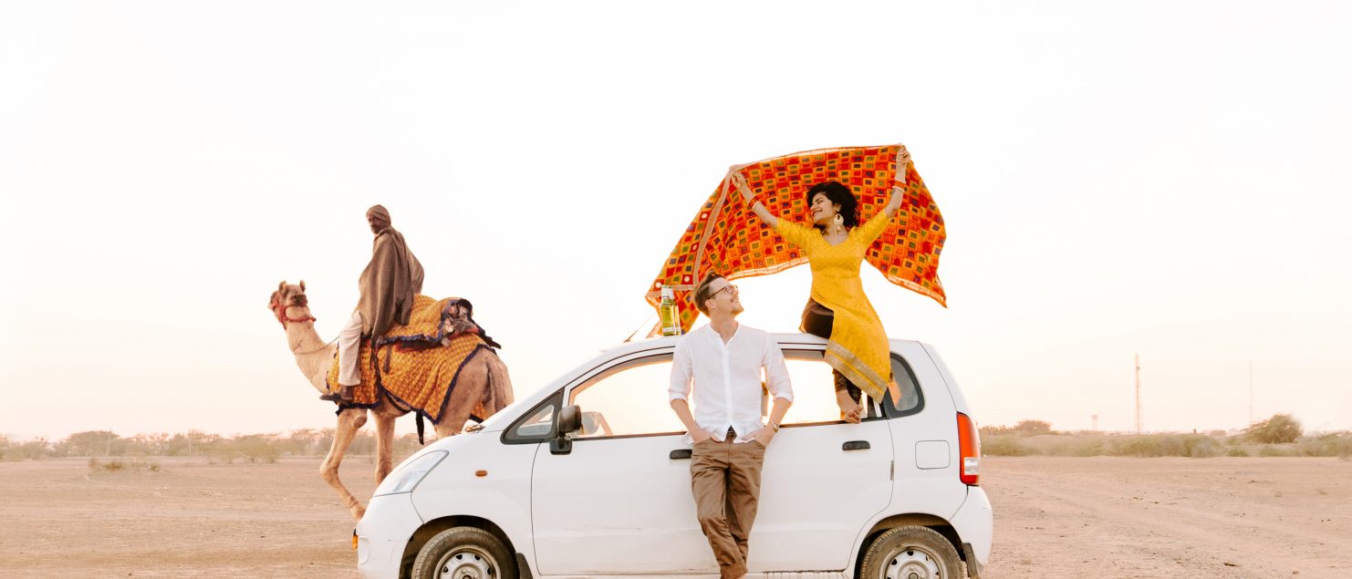 Man and woman leaning on a white car in the desert.